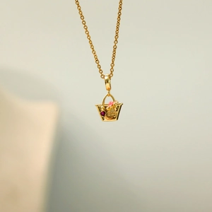Macro detail of a gold basket necklace with red heart stone and BUY text engraving