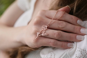Vue rapprochée d'un collier en or rose avec pendentif fleur et papillon sur la main