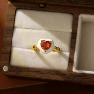 Gros plan détaillé d'une bague coeur dorée avec émail blanc et centre en zircon rouge