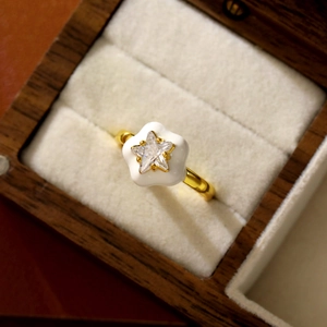Détail d'une bague dorée avec pétales en émail blanc et pierre de zircon en étoile