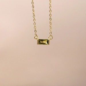 Macro view of a gold pendant featuring a rectangular emerald green zircon stone
