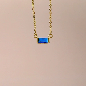 Detailed close-up of a blue rectangular zircon pendant on a delicate gold chain necklace