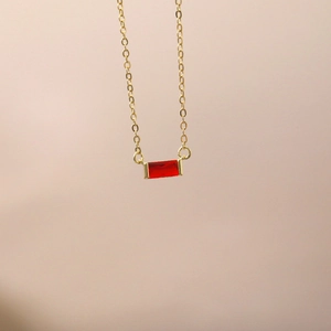 Detailed close-up of a gold necklace featuring a rectangular red zircon birthstone pendant