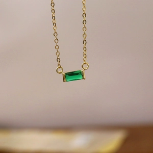 Close-up of a gold chain necklace with a rectangle emerald green stone pendant