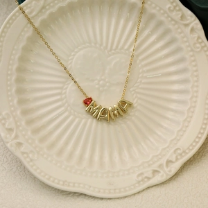 Golden MAMA necklace with red heart birthstone on a ceramic tray for Mother's Day gift
