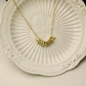 Golden MAMA necklace with a pear-cut birthstone pendant on an elegant white porcelain plate