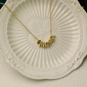 Close-up of gold MAMA necklace with brown birthstone detail on a ceramic dish