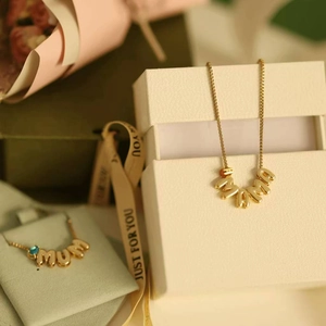 Detailed view of the gold Mama necklace next to a gift box with a Just For You ribbon