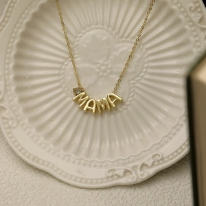 Detail of gold MAMA necklace featuring a light blue teardrop gemstone on a textured dish