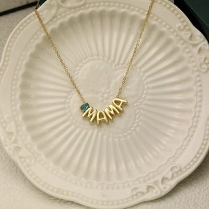 Detail of gold MAMA necklace with blue teardrop gemstone on a white ceramic plate