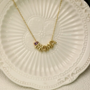 Gold MAMA letter necklace with purple teardrop birthstone pendant on ceramic plate