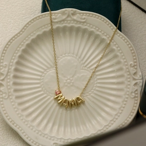 Detail of gold MAMA necklace with pink teardrop birthstone on a ceramic plate