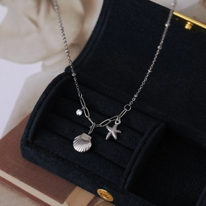 Détail du collier avec pendentifs étoile de mer et coquillage sur boîte en velours bleu