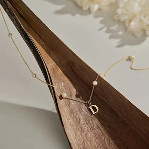 Detail einer goldenen Perlenkette mit einem polierten Buchstaben-D-Anhänger auf einer Schote