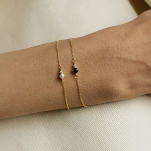 Close-up of gold bracelets with white pearl and black gemstone on wrist with beige background