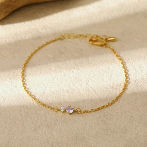 Detail of gold thin chain bracelet featuring white and purple claw-set gemstones