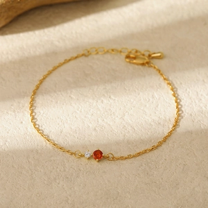 Close-up of gold chain bracelet with orange and clear round birthstone detail
