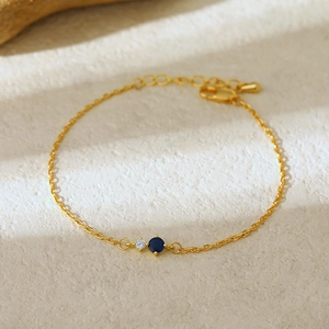 Close-up of gold chain bracelet with blue and white zircons on a textured stone surface