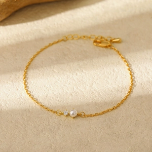 Detailed macro view of minimalist gold chain bracelet featuring a white pearl and zircon