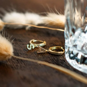 Boucles d'oreilles créoles dorées avec initiales S et A serties de CZ sur fond en bois