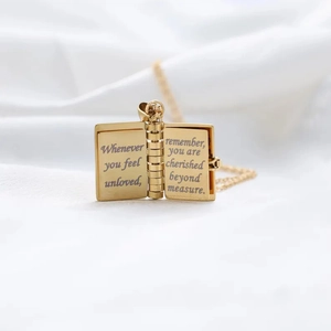 Detail view of open golden book locket necklace with engraved message inside