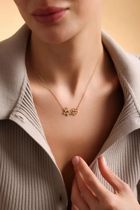 Close-up of gold chain necklace with green and purple flower pendants on a model