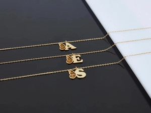 Gros plan de colliers alphabet en acier doré avec pendentifs aile de papillon