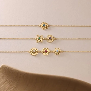 Golden hollow flower and heart necklace with colorful gemstones on a pink surface