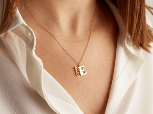 Gros plan d'un collier en titane doré avec pendentif aile de papillon et la lettre E
