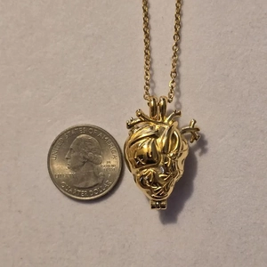 Collana con ciondolo a cuore anatomico dorato mostrata con moneta per dimensione