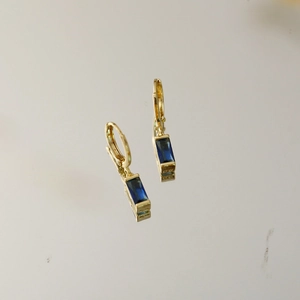 Details von eleganten goldenen Creolen mit rechteckigen dunkelblauen Edelsteinen
