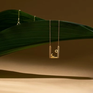 Collier doré avec pendentif soleil et lune sur fond de feuille tropicale verte