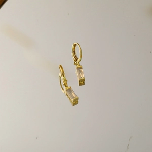 Detail von goldenen Huggie-Ohrringen mit rechteckigem Anhänger auf Spiegeloberfläche