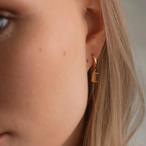 Detailaufnahme goldener Creolen mit rechteckigem grünem Edelstein am Ohr des Models
