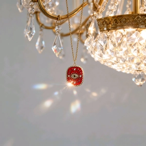 Nahaufnahme einer goldenen Teufelsauge-Halskette mit roter Emaille auf einem Kronleuchter