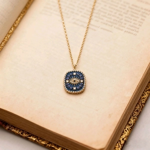 Detail der Vintage Gold-Halskette mit blauem Emaille-Auge auf einer alten Buchseite