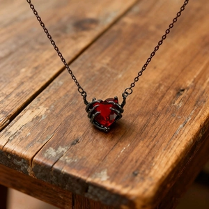 Dettaglio macro del ciondolo a cuore rosso scuro con artigli gotici neri su panca di legno