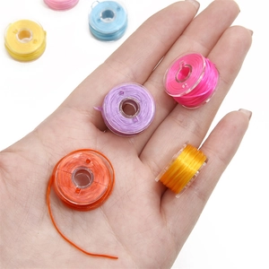 Hand holding 25 color pre-wound sewing bobbins in a clear storage box for DIY crafts