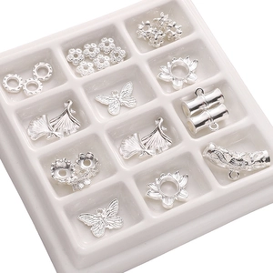 Macro shot of silver-plated lotus and butterfly charms for DIY jewelry making in a white tray