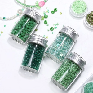 Green glass seed beads in glass bottles for DIY jewelry making sets on white background