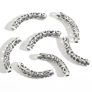 Macro view of vintage silver hollow curved tube beads with intricate floral engraving for DIY