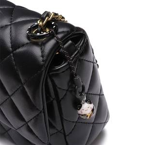 Detail of black quilted shoulder bag featuring gold chain and a lucky cat charm pendant