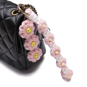 Detail of pink knitted daisy keychain with smile face beads on a quilted leather bag