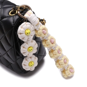 Handmade woven daisy keychain with smiley face charms and gold clasp on a leather bag