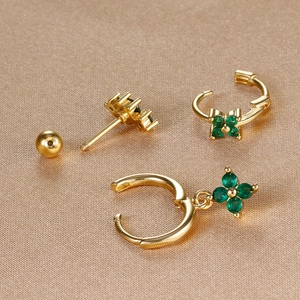 Detailed view of gold clover earrings set with emerald green stones on silk background