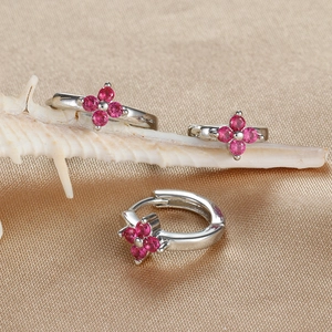 Close-up of three silver clover earrings with pink zircon on silk fabric background