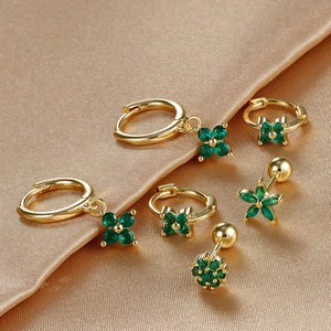 Golden clover earring set with emerald green stones on champagne silk fabric background
