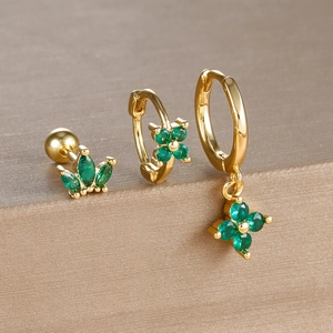 Macro view of gold four-leaf flower and crown earrings set with green gemstones