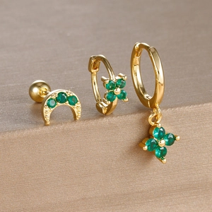 Detailed close-up of gold clover earrings set with green stones on a textured display
