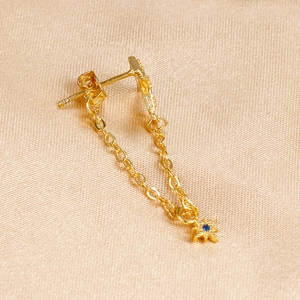 Detail of gold chain earring with star pendant and blue zircon on silk background